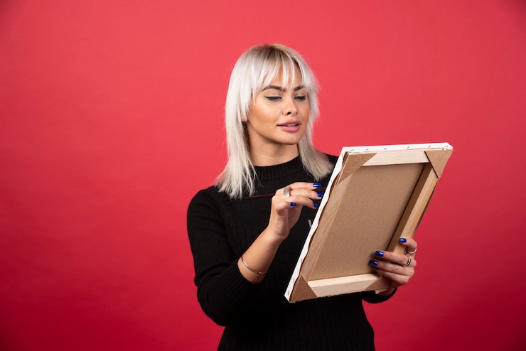 Photo gratuit femme jeune artiste dessin sur toile sur un mur rouge.