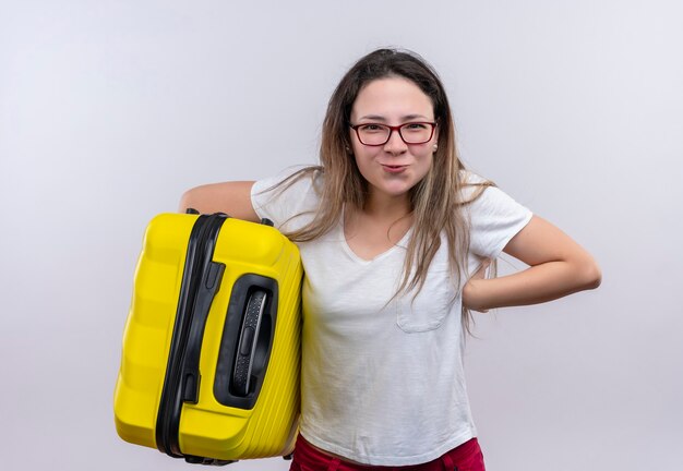 Femme jeune voyageur en t-shirt blanc tenant la valise à la joyeuse et heureuse souriant debout sur un mur blanc