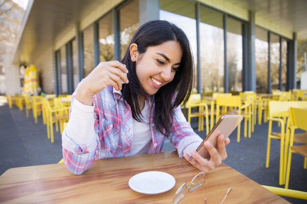 Femme joyeuse à l&#39;aide de smartphone et de boire du café au café