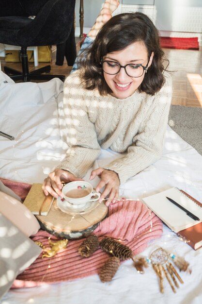 Femme joyeuse avec boisson allongée sur le lit