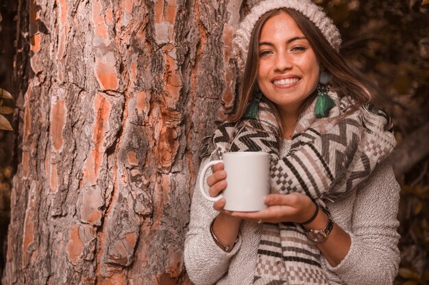 Femme joyeuse avec boisson près de l&#39;arbre