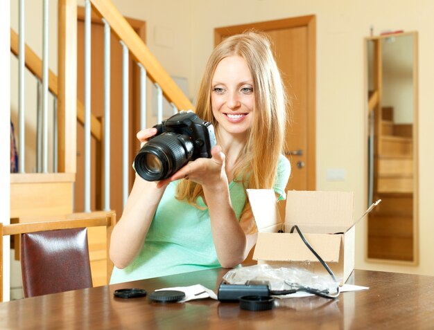 femme joyeuse avec les cheveux blonds déballage pour nouvel appareil photo numérique à la maison