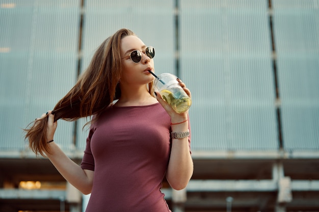 Femme joyeuse dans la rue, boire une boisson rafraîchissante le matin