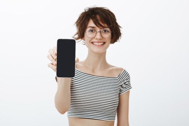 Femme joyeuse hipster présente l'application, montrant l'écran du smartphone