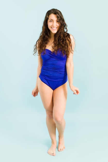 Femme joyeuse avec un maillot de bain bleu sur le point d'entrer dans une piscine en été. Heureuse jeune femme souriante pendant ses vacances d'été