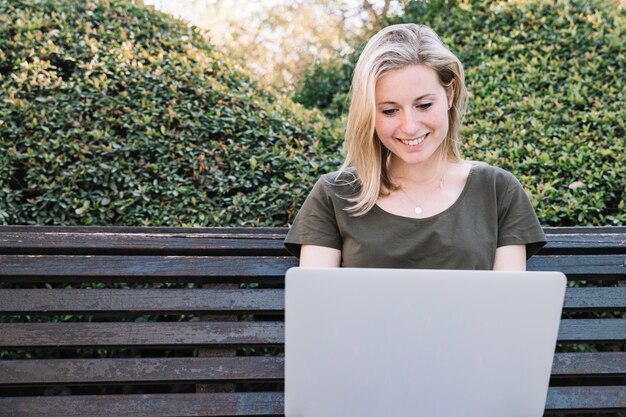 Femme joyeuse, navigation sur ordinateur portable sur banc