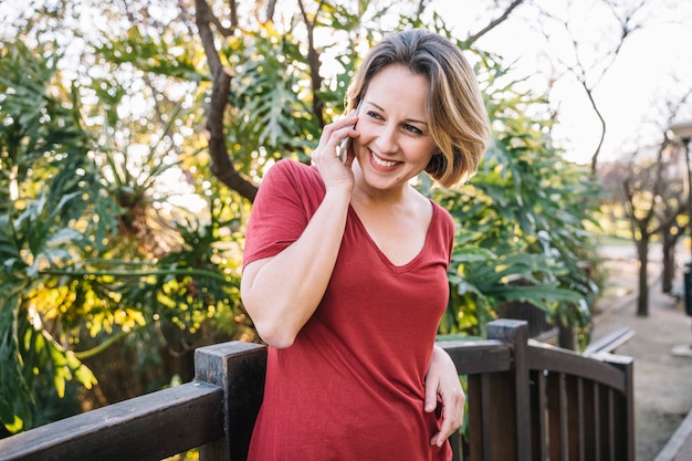 Photo gratuite femme joyeuse, parler au téléphone près de clôture