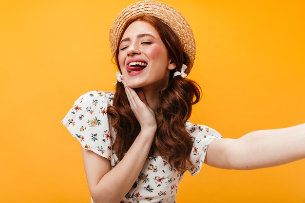 Femme joyeuse en plaisancier montre sa langue et pose pour selfie sur fond orange.