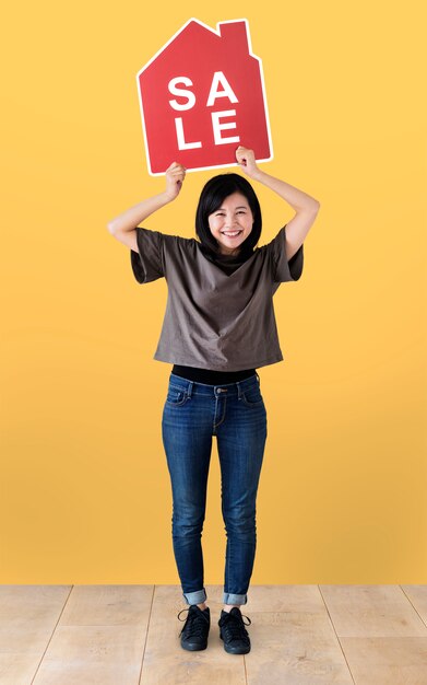 Femme joyeuse tenant une icône de vente de maison