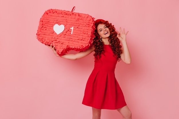 Photo gratuite femme joyeuse en tenue rouge minimaliste sourit et montre le signe ok. fille au béret tient comme signe sur l'espace rose.