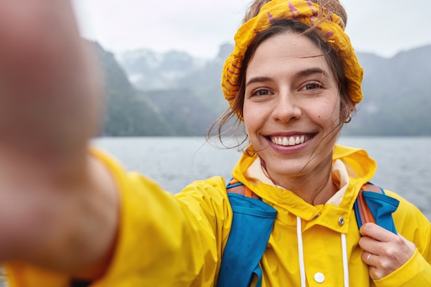Une femme joyeuse a une tournée d'expédition, fait un portrait en selfie, s'étire la main à huis clos, sourit largement
