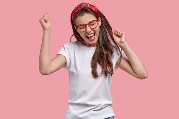 Une femme joyeuse triomphante serre les poings, se réjouit des nouvelles positives, s'exclame joyeusement, modèles sur l'espace rose