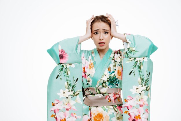 Femme en kimono japonais traditionnel confus et déçu se tenant la main sur la tête sur blanc