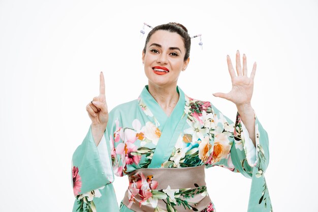 Femme en kimono japonais traditionnel heureux et positif montrant le numéro six avec les doigts sur blanc