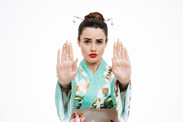 Femme en kimono japonais traditionnel avec un visage sérieux faisant un geste d'arrêt avec les mains sur blanc