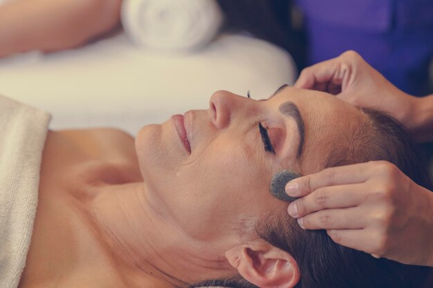 Femme latine d'âge moyen allongée sur des lits de massage dans le luxueux spa, massage aux pierres