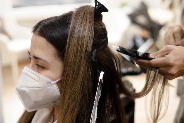 Femme latine aux cheveux longs dans le salon de coiffure avec masque et mains du coiffeur sélectionnant les serrures pour la peinture