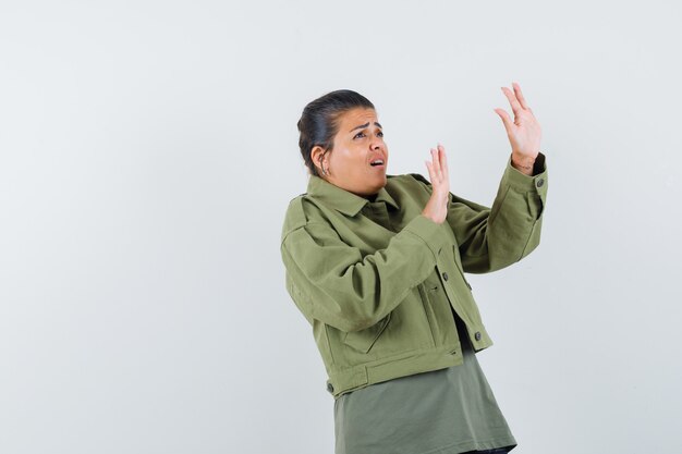 Femme levant les mains de manière protectrice en veste, t-shirt et à la peur.