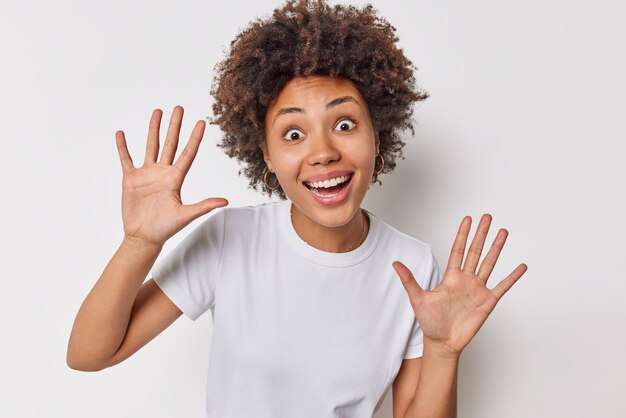 la femme lève les paumes sur la caméra sourit positivement a une expression joyeuse porte des vêtements décontractés pose contre le blanc. Concept de personnes et de bonheur