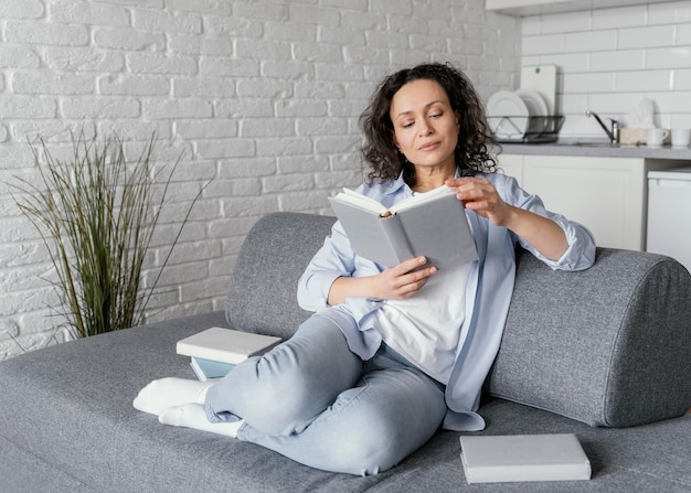 Femme lisant sur le canapé plein coup