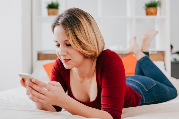 Femme sur le lit en utilisant un smartphone