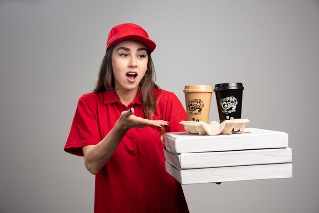 Femme de livraison choquée regardant la pizza et les tasses à café sur le mur gris.