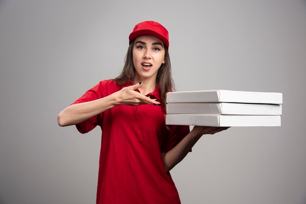 Femme de livraison montrant des pizzas sur un mur gris.