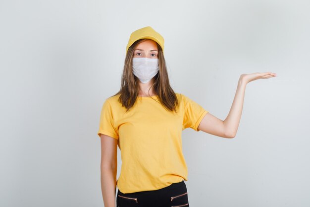 Femme de livraison montrant quelque chose avec la main en t-shirt, pantalon, casquette et masque