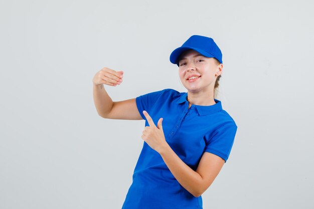 Femme de livraison pointant sur ses doigts pliés en t-shirt bleu et casquette et à drôle