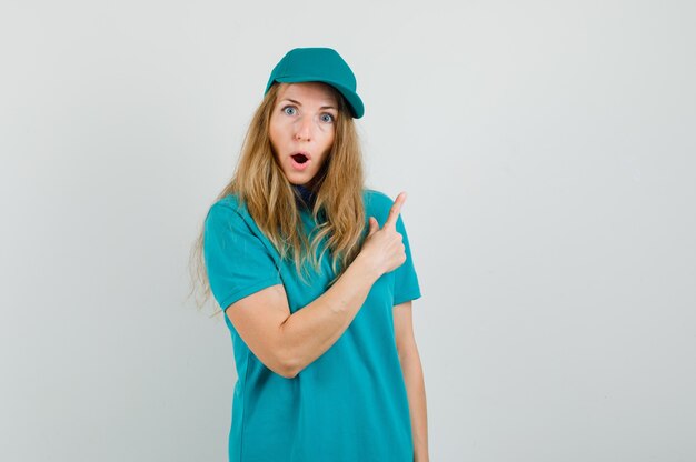 Femme de livraison pointant vers l'extérieur en t-shirt, casquette et à la surprise