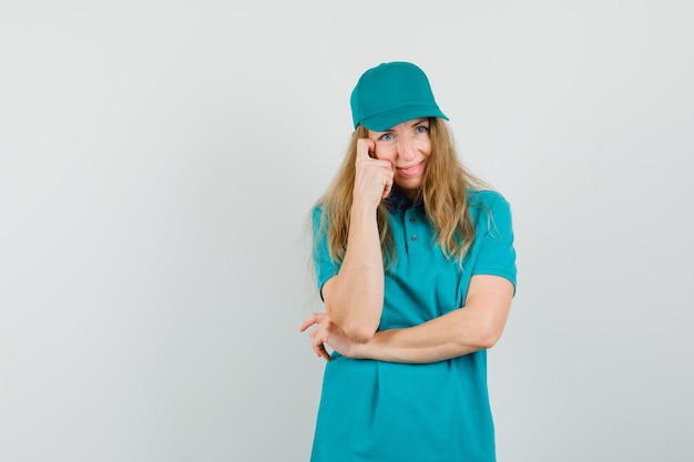 Femme de livraison en t-shirt, casquette debout dans la pensée pose et à la bonne humeur