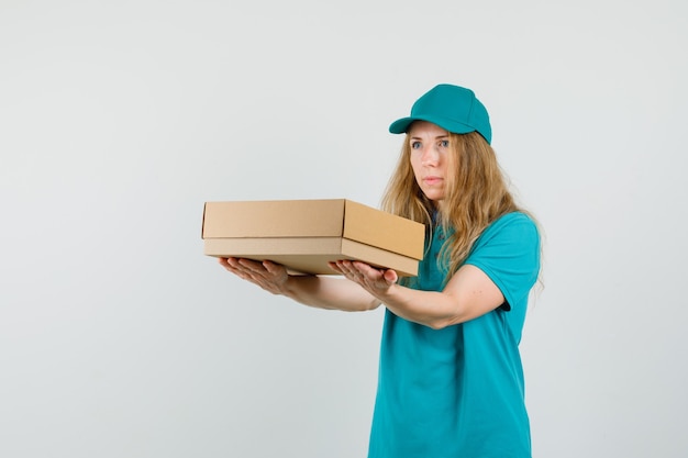 Femme de livraison en t-shirt, casquette livrant une boîte en carton