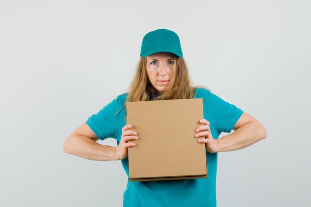 Femme de livraison en t-shirt, casquette tenant une boîte en carton