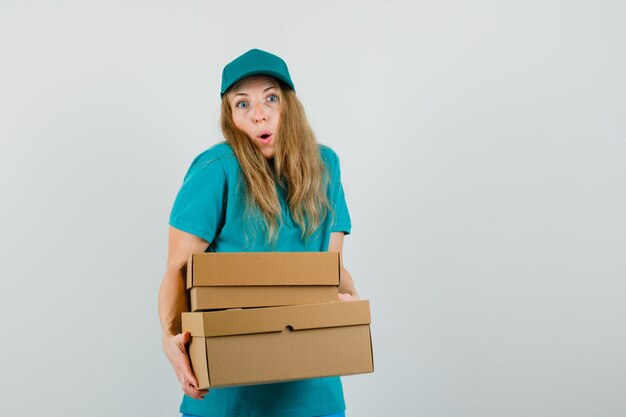 Femme de livraison en t-shirt, casquette tenant des boîtes en carton et à la surprise