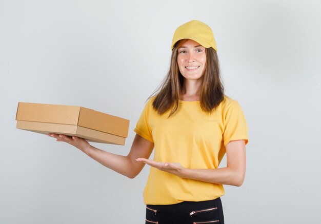 Femme de livraison en t-shirt jaune, pantalon, casquette montrant la boîte en carton et à la joie