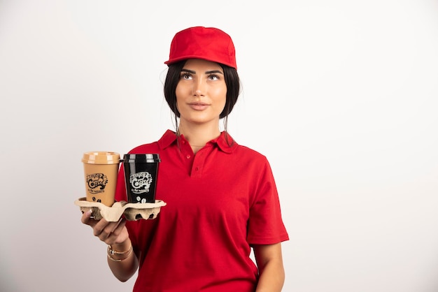 Femme de livraison avec des tasses à café posant sur fond blanc. Photo de haute qualité