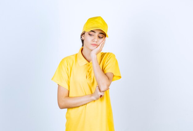 Femme de livraison en uniforme jaune debout et regardant vers le bas.