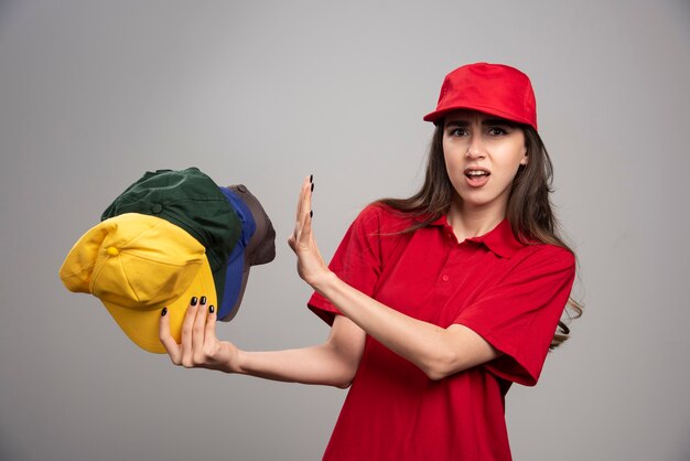 Femme de livraison en uniforme rouge à l'écart des casquettes colorées.