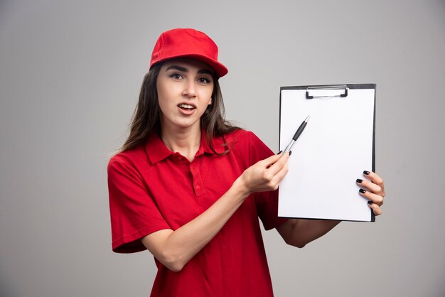 Femme de livraison en uniforme rouge pointant sur le presse-papiers.