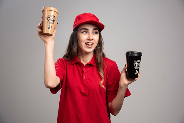 Femme de livraison en uniforme rouge tenant des tasses à café.