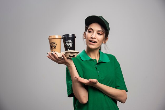 Femme de livraison en uniforme vert debout avec des tasses de café.