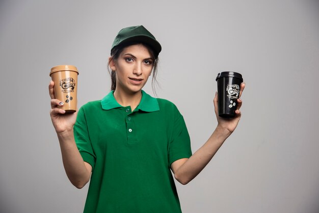 Femme de livraison en uniforme vert posant avec un délicieux café.