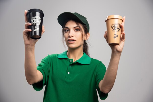 Femme de livraison en uniforme vert posant avec des tasses à café