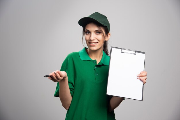 Femme de livraison en uniforme vert tenant le presse-papiers.