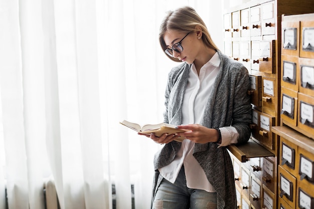 Photo gratuite femme avec livre s'appuyant sur le catalogue de la bibliothèque