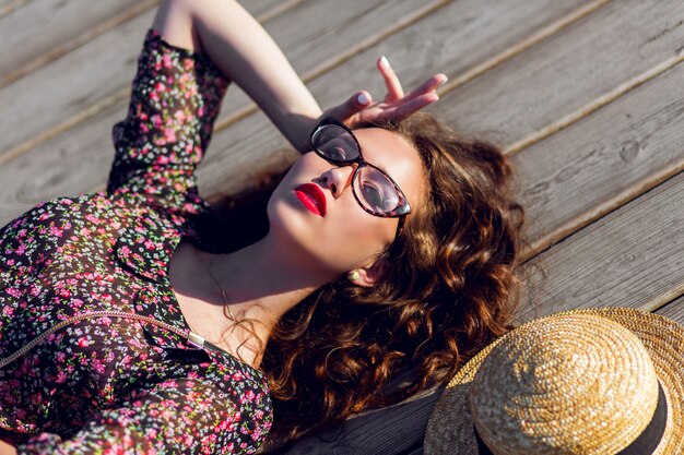 Femme en longue robe colorée et chapeau de paille portant allongé sur le plancher en bois