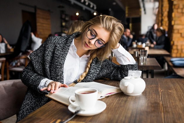 Photo gratuite femme à lunettes, lecture de livre au café