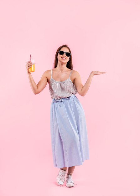 Femme à lunettes de soleil debout et tenant un verre de jus