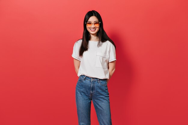 femme en lunettes de soleil orange sourit sur le mur rouge