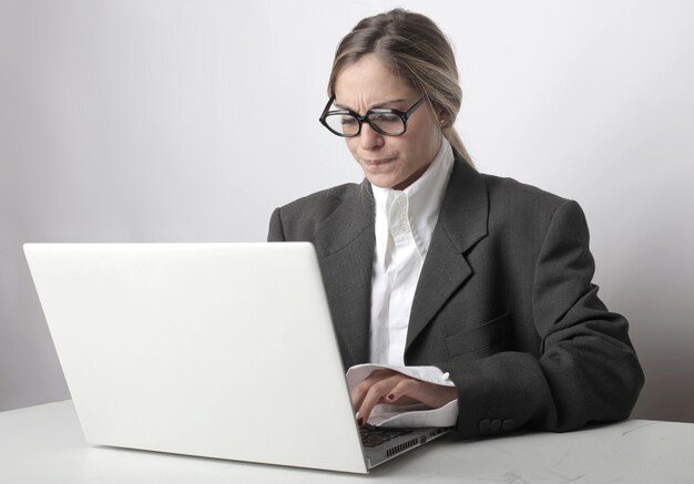 Femme avec des lunettes et un visage inquiet travaillant sur son ordinateur portable au bureau